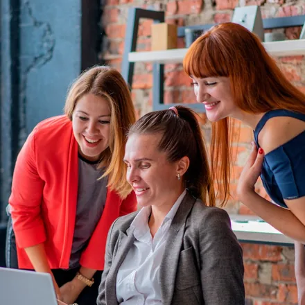 Três colegas de trabalho sorrindo em frente a um computador