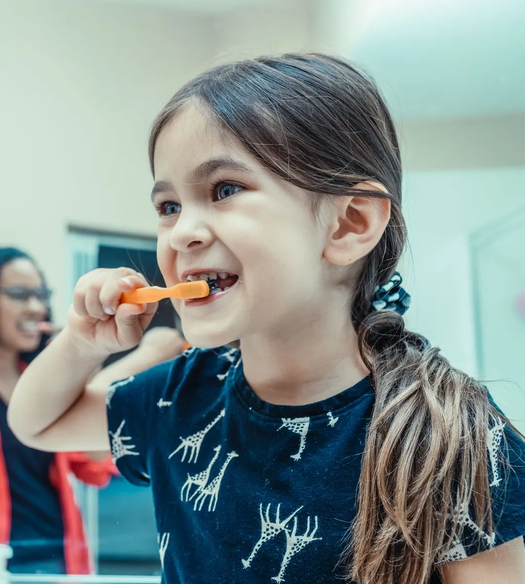 Menina sorrindo enquanto escova os dentes com uma escova laranja